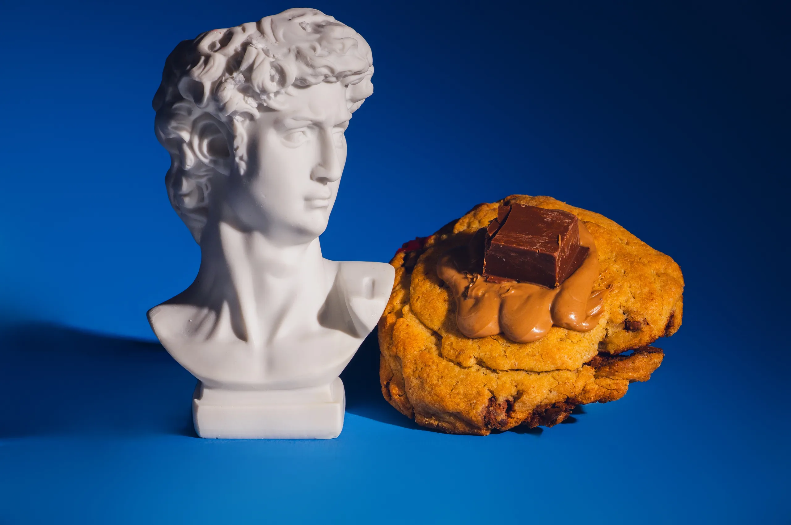 Cookie Hestia au chocolat à côté d’un buste grec sur fond bleu